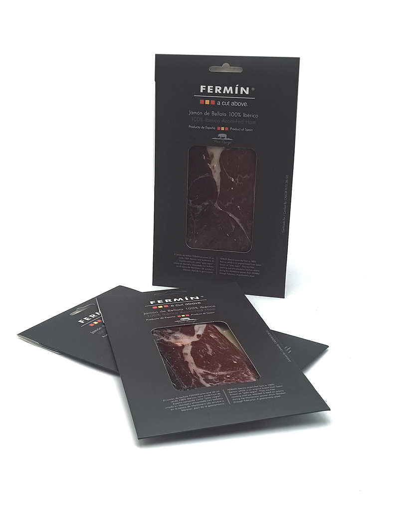 1777484622524 - El Gourmext de Casa Chino Dark packaging for Fermín 100% Ibérico ham with a transparent window showing sliced meat; several packages standing and one upright, product branding visible.