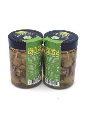Two glass jars of green olives with blue lids, green labels reading La Gilda de Norte, placed side by side.