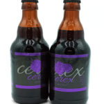 Two brown glass beer bottles with purple labels featuring a grape illustration, standing side by side on a white background.
