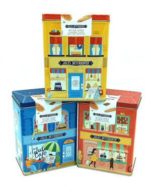 Three colorful tin containers shaped as stylized shopfronts stacked together, each displaying Jules Destrooper branding and product names like butter crisps, almond thins, and butter waffles.