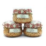 Three glass jars of Fabada Asturiana beans sealed with red plaid lids, stacked in a pyramid, ready for sale.