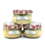 Three glass jars of Cardo con almendras arranged in a triangle, with red plaid cloth lids and white labels.
