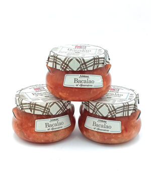 Three small glass jars of Bacalao (salt cod) in red sauce, topped with patterned cloth lids, arranged in a pyramid on a white background