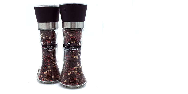 Two clear pepper mills filled with mixed peppercorns standing side by side on a white background.