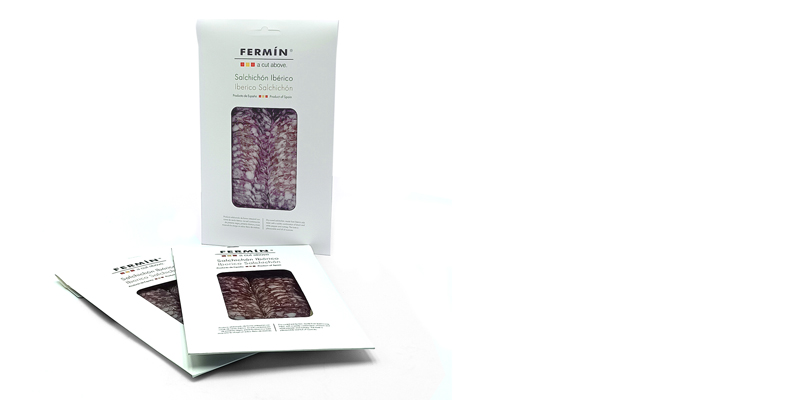 Boxed Fermín ibérico salchichón with a clear window showing cured meat, standing on a white background, with two flat packets nearby