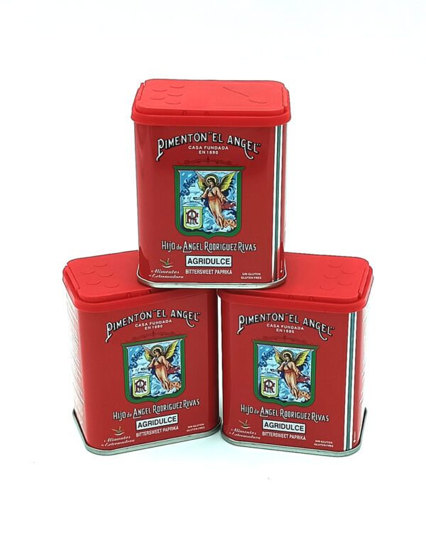 Three red paprika tins with red lids stacked together, label showing a crest and 'Pimentón El Angel' branding (Agrudulce).
