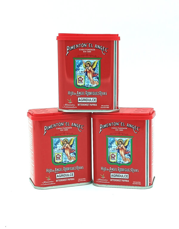 Three red metal tins of Pimentón 'El Ángel' stacked together, featuring an angel emblem and 'AGRIDULCE' on the front label.