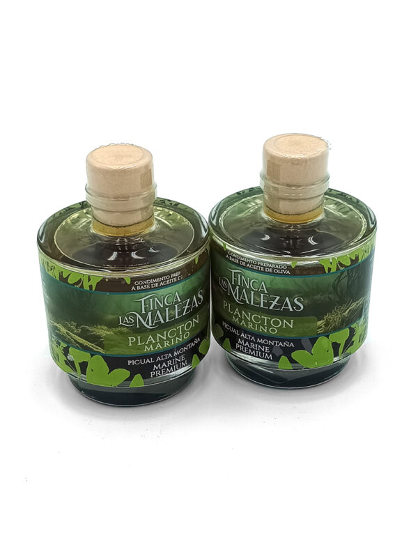 Two small glass bottles with cork stoppers, green plant-themed labels, likely olive oil or marine condiment, displayed on a white background.
