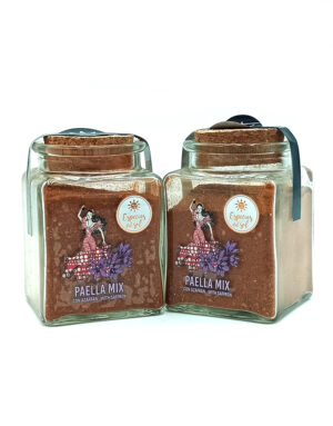 1776794963921 - El Gourmext de Casa Chino Two square glass jars with cork lids containing paella mix, labeled 'Paella Mix' with saffron and azafrán, placed side by side on a white background.
