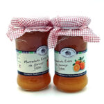 Two glass jars of orange marmalade with red checkered cloth lids tied with string.