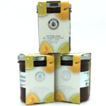Three boxes of apricot jam with lime arranged around a glass jar on a white background.