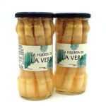 1778794818791 - El Gourmext de Casa Chino Two glass jars with black lids labeled La Huerta de La Vera, filled with light brown pickled peppers side by side on a white background, front labels visible.